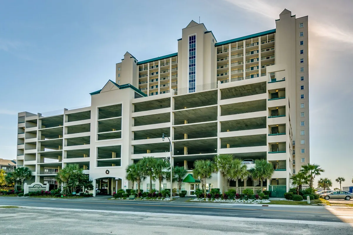 The image captures the modern exterior of the condominium, showcasing its architectural design, inviting landscaped entrance, and ample parking area. The building's facade appears welcoming and accessible, creating a sense of arrival for group travelers.