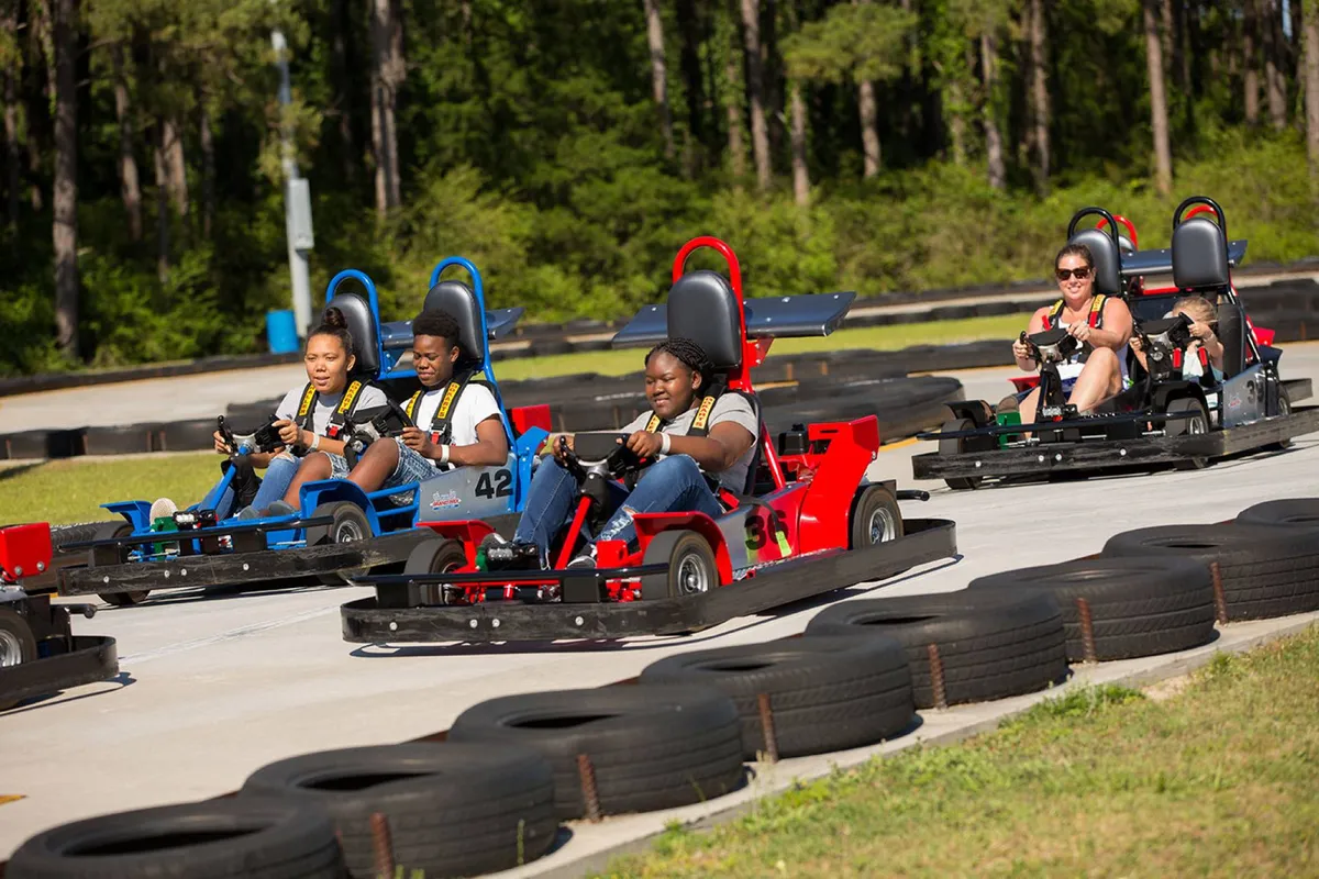 An energetic outdoor scene featuring a go-kart track, participants racing, and a playful, competitive environment. The bright setting and visible excitement of the racers suggest fun for families and groups.