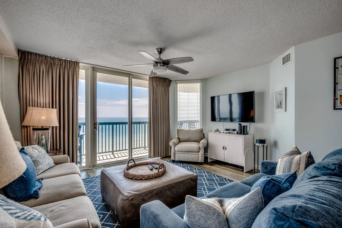 The image showcases a bright, inviting living area with plush, comfortable seating arranged around a stylish round coffee table. Massive windows reveal breathtaking ocean views, filling the space with natural light and offering a front-row seat to stunning sunsets. The setting exudes a cozy, tranquil vibe perfect for relaxing, enjoying family movie nights, or sharing conversations with friends.