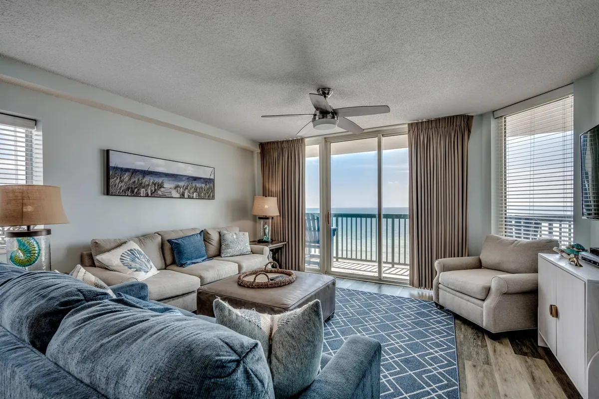 A calm and inviting living room featuring a comfortable sofa adorned with decorative throw pillows, a coffee table, tasteful artwork on the wall, and, most prominently, large windows framing a breathtaking ocean view. Natural light fills the space, and the setup invites relaxation and togetherness.