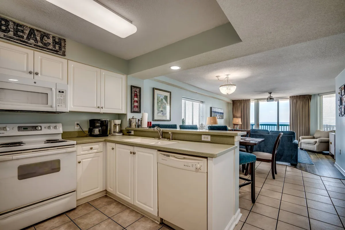 A bright, open-concept living area with a kitchen counter that flows into the living space, featuring large windows that offer expansive ocean views. The setting suggests a seamless transition between indoor comfort and the allure of the outdoors, ideal for gathering before or after a day of exploration.