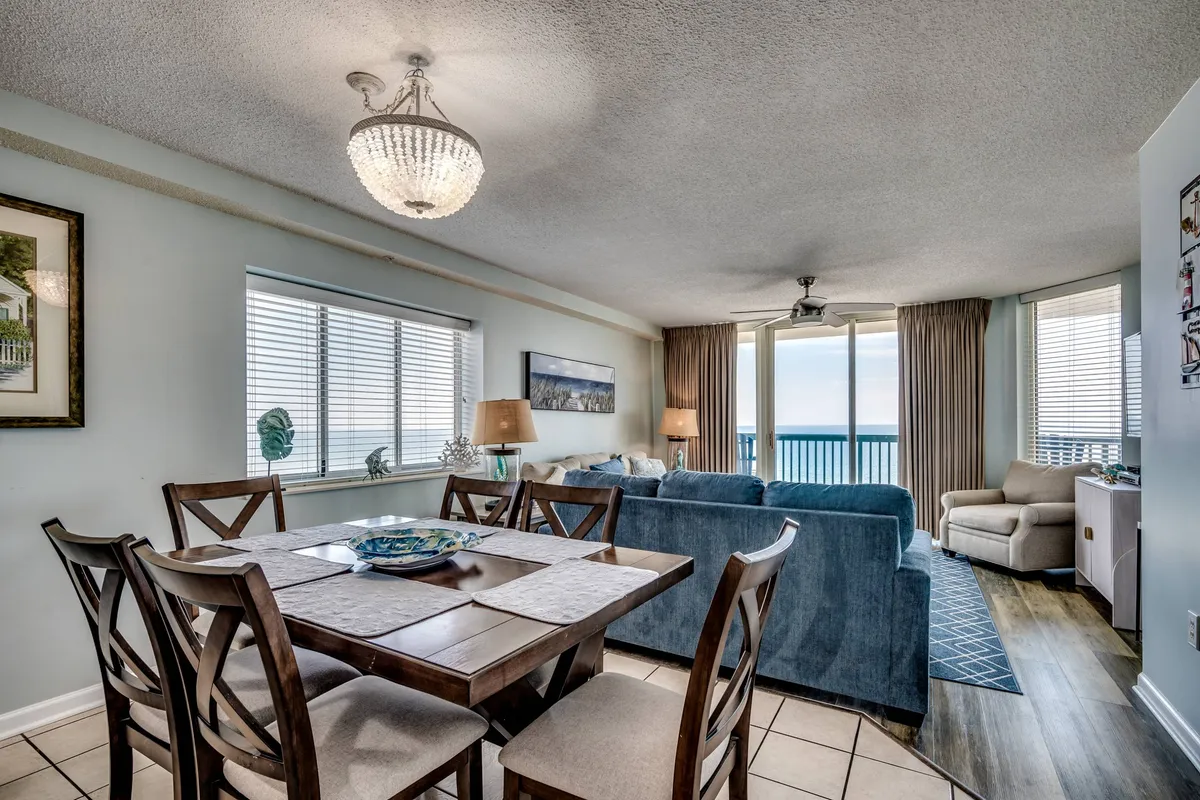 A spacious, open-concept area combining a dining table, a cozy sofa, and grand windows that overlook the ocean. A chandelier adds elegance, while the natural light streaming through the windows enhances the inviting vibe. The setting is ideal for family meals, entertaining, or simply enjoying the view together.
